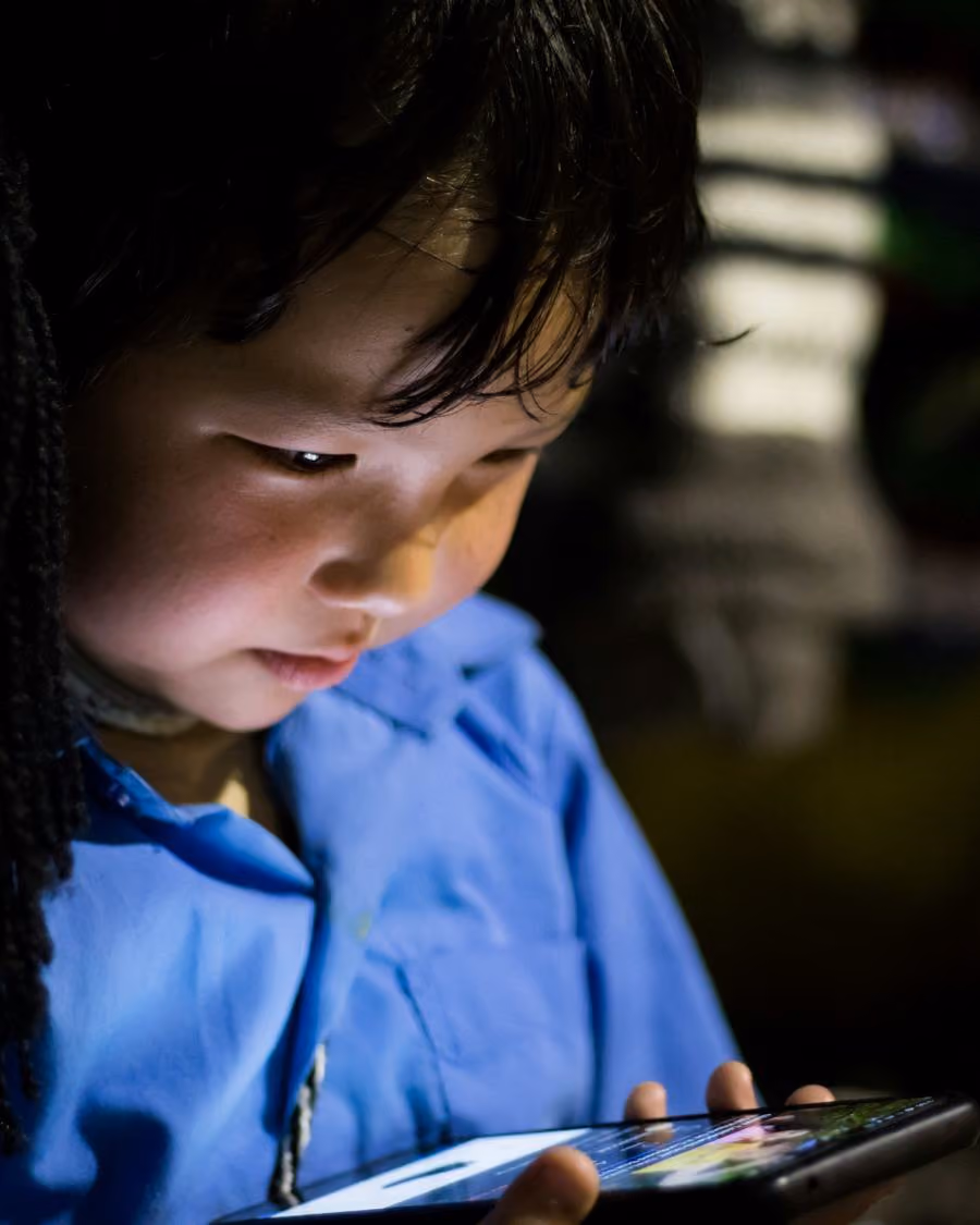 Criança segurando um tablet com o rosto iluminado pela tela