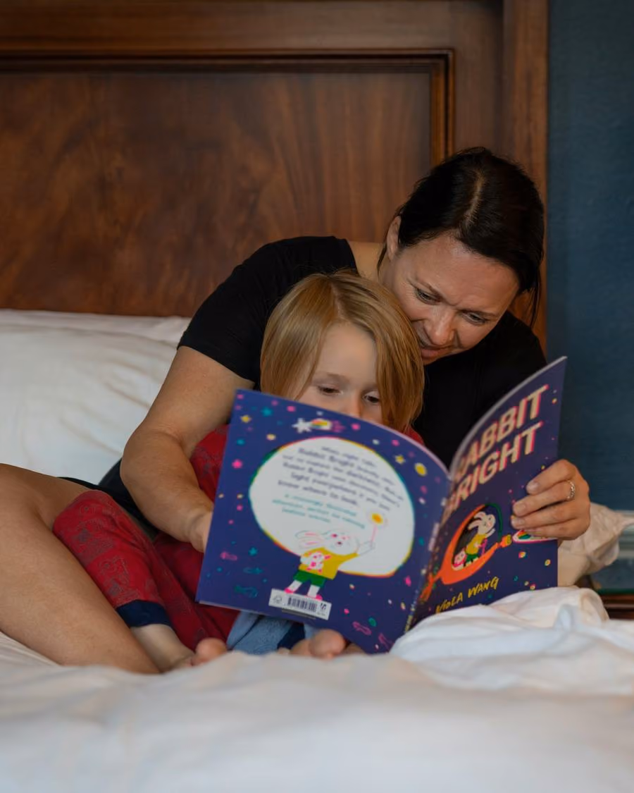 Mãe e filha deitadas lendo uma história na cama